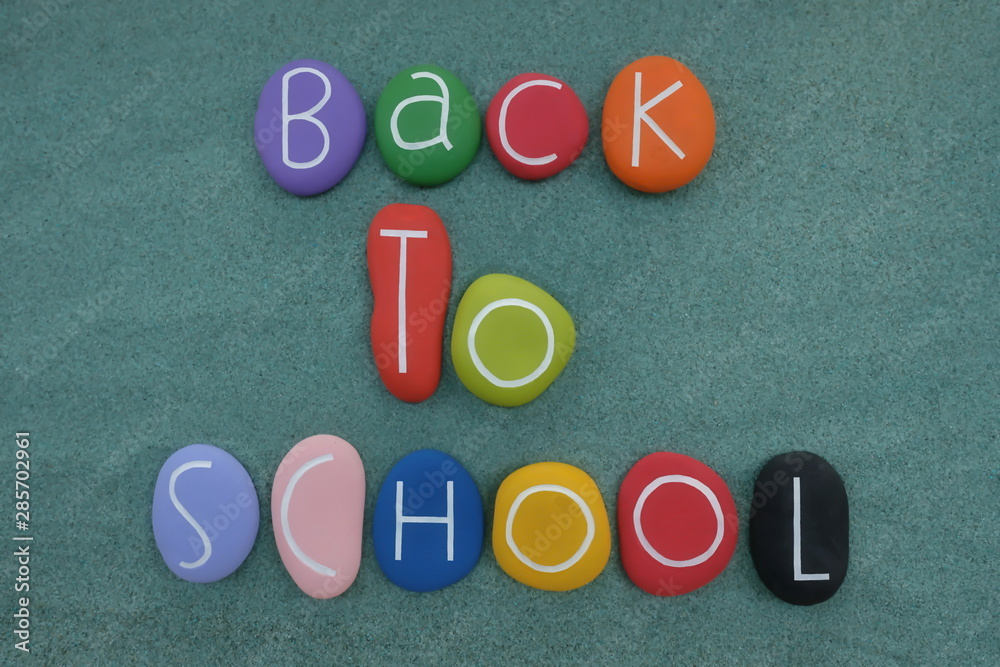 Wall mural back to school text composed with multi colored and carved stones over green sand