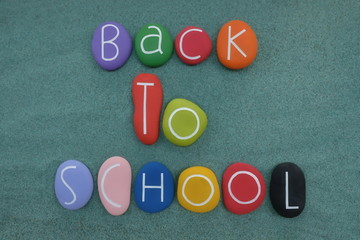 Back to School text composed with multi colored and carved stones over green sand