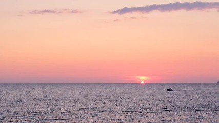 Sunset over the sea. The setting sun and the dark silhouette of a motor boat floating on its background