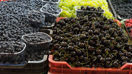 Mix of organic fruit in plastic box at local market ready to sell. Seasonal products in container in supermarket. Blackberry, cherry and grapes.