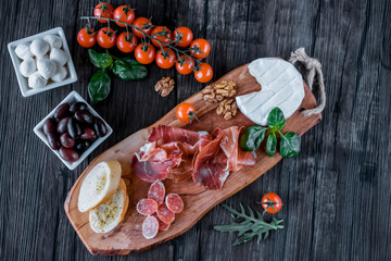 Prosciutto, bread, olives, walnut, mozzarella, salami, basil and cherry tomatoes on  brown wooden board.  Mediterranean kitchen. Top view.