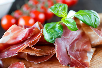 Prosciutto, bread, olives, walnut, mozzarella, salami, basil and cherry tomatoes on  brown wooden board.  Mediterranean kitchen. Top view.