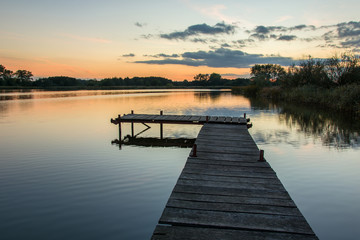 Fototapeta na wymiar A pier on a calm lake and the sky after sunset