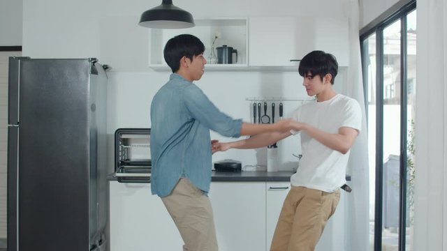 Asian Gay couple dancing at home. Young Asian LGBTQ men feeling happy fun dance, singing, listening music while in kitchen at home concept. Slow motion Shot.