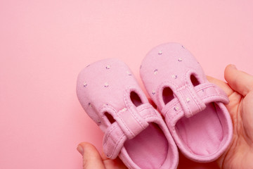 Girl's Baby textile Slippers in a hands female on pink background with copy space.