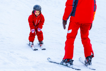 Fototapeta na wymiar Professional ski instructor is teaching a child to ski on a sunny day on a mountain slope resort with sun and snow. Family and children active vacation.