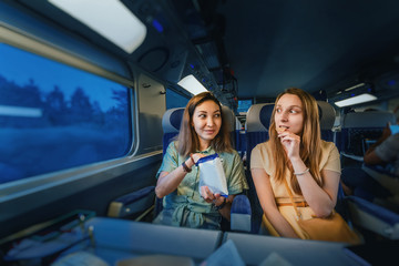 Two girl friends passengers sitting in first class train at night time, and eating chips © EdNurg