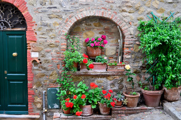 Fototapeta na wymiar Flowerpots with plant and colorful flowers in front of a brick wall, in Tuscany, Italy