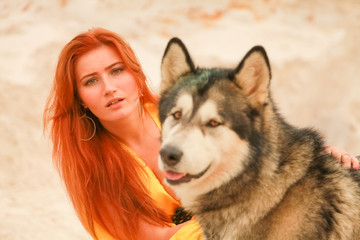 Young long hair woman posing with her dog alaskan malamute in the sand desert