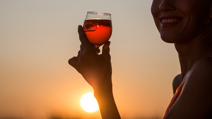 Happy brunette woman holding iced aperol spritz over sunset sky