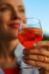 Summer cocktails. Cheers, woman holding cocktail, aperol in the hand outdoors over blue sky, focus on hand with a glass