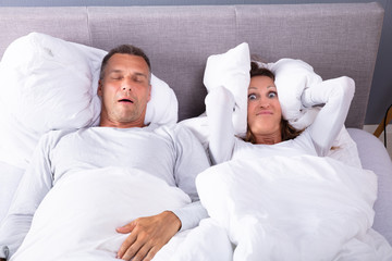 Woman Covering Her Ears With Pillow Near Snoring Man