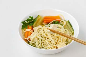 Traditional asian soup with tofu cheese, noodles, carrots and zucchini on white background. This dish usually contains bouillon and vegetables