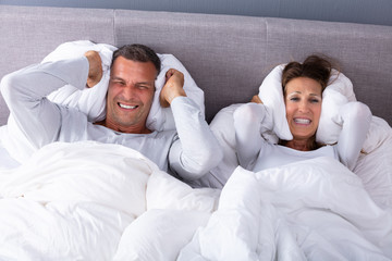 Disturbed Couple Covering Their Ears With Pillow On Bed
