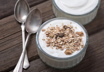 White yogurt in glass bowl on old wooden desk with two old rustic spoons.