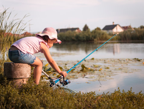 Sweet little girl on fishing near the river. Little girl, 4-5 years, spending fishing time alone on the river coast. Kids and fishing concept.