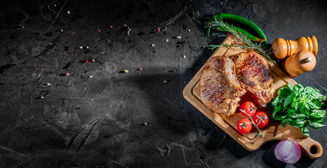 Grilled steak with herbs, spices and cherry tomatoes on dark background. Top view with copy space