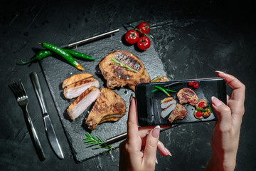 Hands taking photo a grilled steak with herbs, spices on a dark background with smartphone