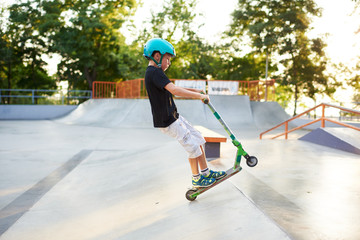 A boy on a scooter and in protective helmet do incredible stunts in skate park. Extreme jump. The concept of a healthy lifestyle and sports leisure