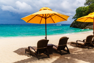 Sun umbrella and beach beds under the palm trees on tropical beach. Summer vacantion concept.