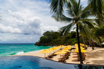 Umbrella from the sun, beach beds, infinity pool, under palm trees on a small sandy beach on a tropical island. The concept of summer vacation.