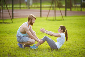 Naklejka na ściany i meble Sit ups fitness couple exercising sit up outside in grass. Fit people working out cross training. Woman doing abdominal crunches press exercise with trainer. Couple Doing Sit-Ups Abdominal Crunch