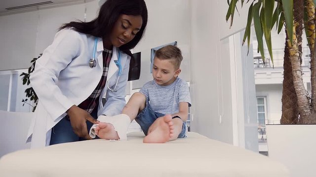 Young female doctor removing bandage from leg of little patient.