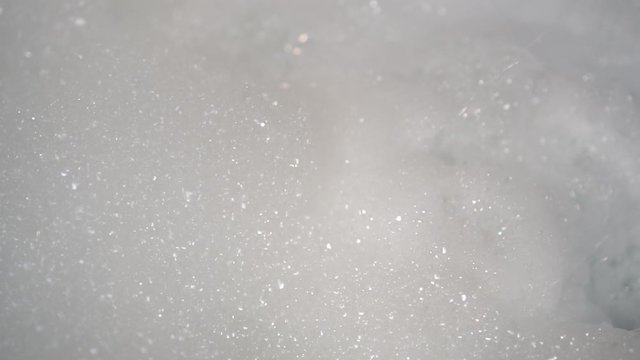 A stream of water from the shower blurs a bunch of foam into the bathtub. Bubbles form and fall. Use of hygiene products