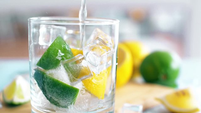 Close up of fresh summer drink with lime, lemon and ice cubes with water splashing intro glass. Slow motion footage.