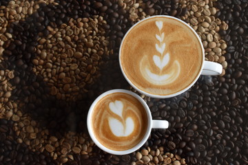 Top view of Regular latte (210-220 ml.) and Piccolo latte (90-100 ml.) with milk foam art in white cups on coffee beans table, caffeine concept.