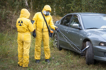 Two dosimetrist  in protective suite and mask with geiger counter measuring radiation level near car - 285729106