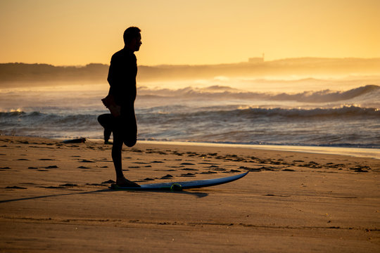 A surfer is stretching and getting ready to surf the waves at a beach