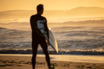 Surfer walking observing the surf on a beach at sunrise