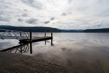 Lake Maraetai in Mangakino, Waikato district, New Zealand. Still waters, small boat jetty, reflections of cloud and sky. Moody, peaceful, reflective. Hydroelectric station, recreational activities.