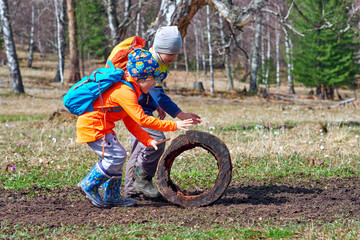 Hiking children with backpacks play with a stump, roll it like a wheel