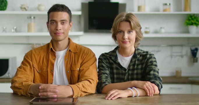 Portrait of young successful mixed race couple, sitting at table in kitchen, looking confident and happy, wearing casual clothes. Hispanic, latin, Caucasian, white. 4K, RED camera.