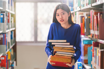 Asian young Student in casual suit holding after searching the book from book shelf in library of university or colleage with various book background, Back to school concept