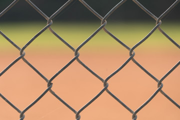 Close up picture of chain link fence with blurred baseball field in background.