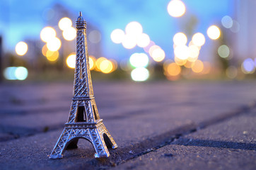 Eiffel tower figure on a background of evening bokeh lights. Located on the paving stones, asphalt.