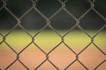 Close up picture of chain link fence with blurred baseball field in background.