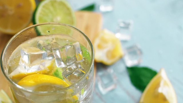 Close up slow motion of ice falling intro glass with slice lime and lemon. Fresh coctail stay on chopping board. Summer drink.