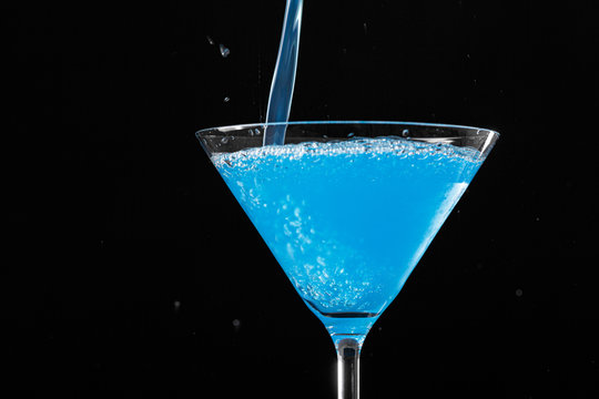 Blue Cocktail Pouring In A Martini Glass On Black Background. Copy Space