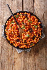 Tasty fried chickpeas with eggplant in tomato sauce close-up on a plate on the table. Vertical top view