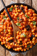 Israeli vegetarian cuisine stew of chickpeas with eggplant, tomatoes, onions and spices closeup on a plate. Vertical top view