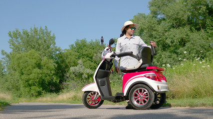 Woman standing near an electric scooter in the city park. Concept of driving ecological environmentally conscious power transport. Active adult lifestyle.