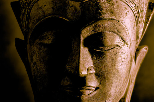 Buddhism. High contrast Buddha face statue close-up. Dramatic side light