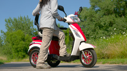 Woman standing near an electric scooter in the city park. Concept of driving ecological environmentally conscious power transport. Active adult lifestyle. © desertsands
