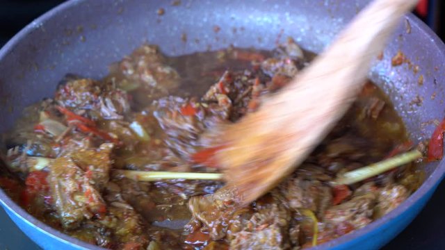 Frying pan with onion, lemongrass, red pepper and beef meat, close up. Indonesia. Sambal Goreng Ati Kentang, Indonesian cuisine, spicy beef meet and potatoes garnish with lemongrass leaf and red chili
