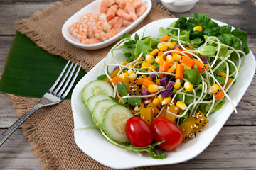 Fresh salad plate with shrimp, salmon, tomato and mixed greens  on wooden background .