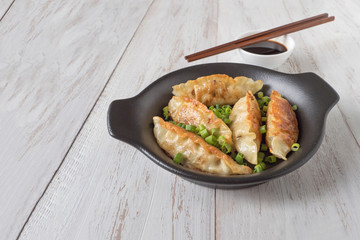 Fried Asian dumplings in bowl, chopsticks, rustic wood background. Chinese dumplings for dinner.